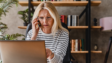 Una mujer mirando una computadora portátil mientras habla por teléfono móvil